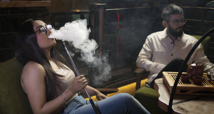 A girl is smoking and a man is sitting 